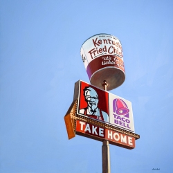 A tall signpost featuring a large KFC bucket on top and below it, KFC and Taco Bell logos with the text "TAKE HOME.