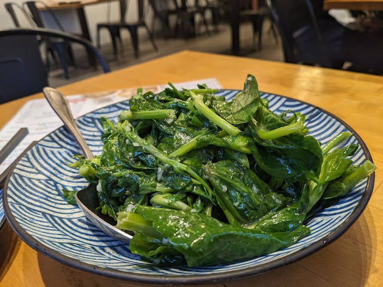 A plate of sautéed leafy greens served on a blue and white patterned dish with a spoon.