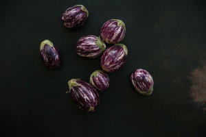 Seven purple-and-white striped eggplants spread on a dark green surface.