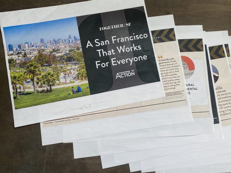 A stack of printed documents features a cover with an image of San Francisco and text reading "A San Francisco That Works For Everyone" and "TOGETHER SF ACTION.