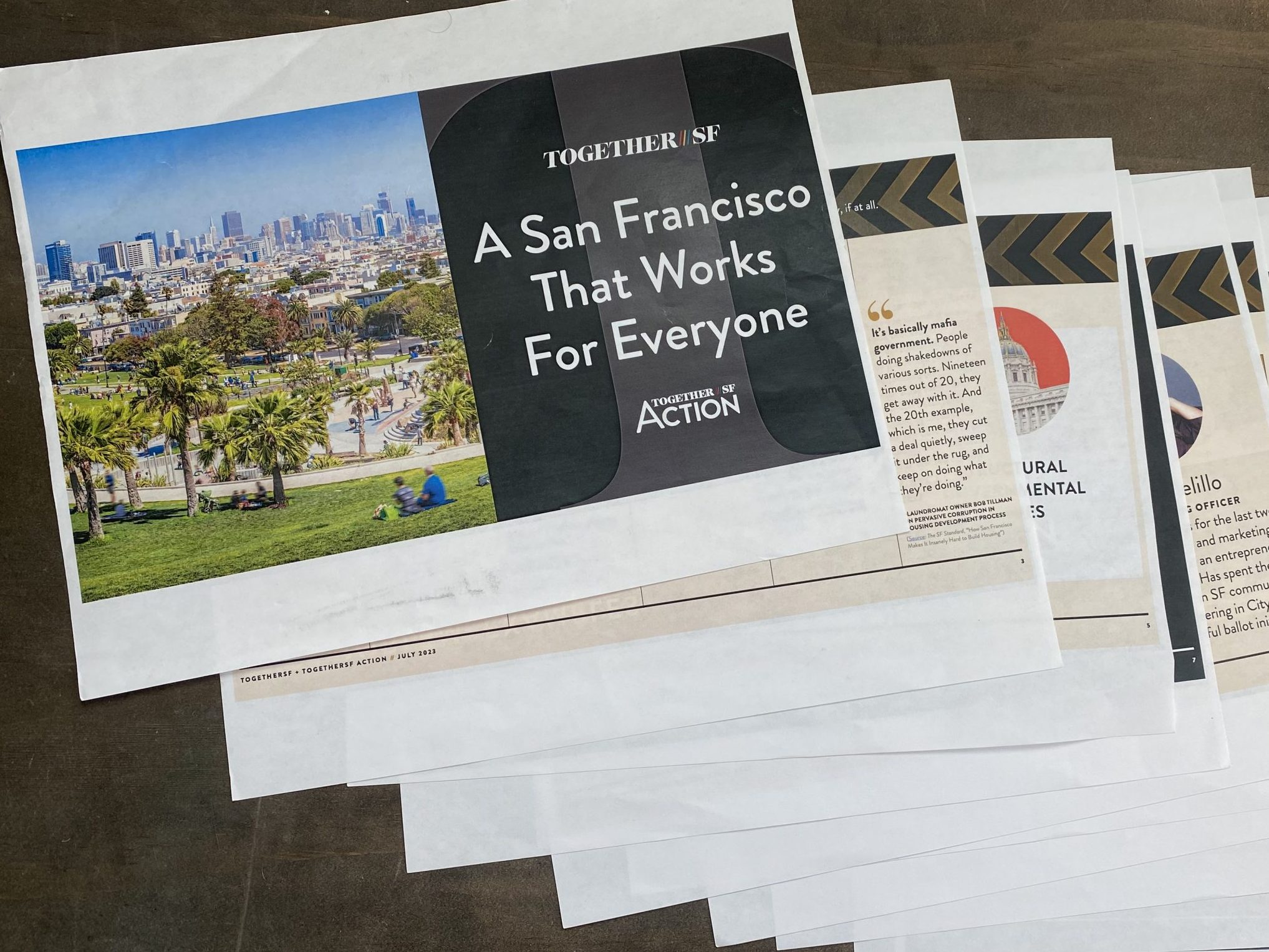 A stack of printed documents features a cover with an image of San Francisco and text reading "A San Francisco That Works For Everyone" and "TOGETHER SF ACTION.