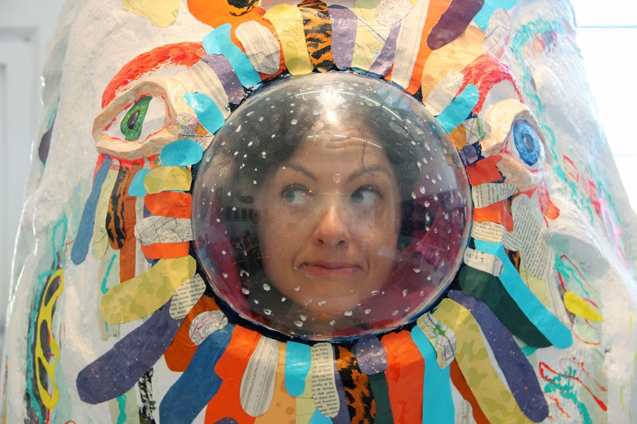 A person looks through a circular window in a colorful, abstract installation with various patterns and textures surrounding the window.