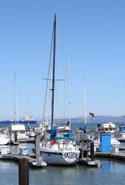 A sailboat named "Taylor" docked at a marina with several other boats on a clear, sunny day.