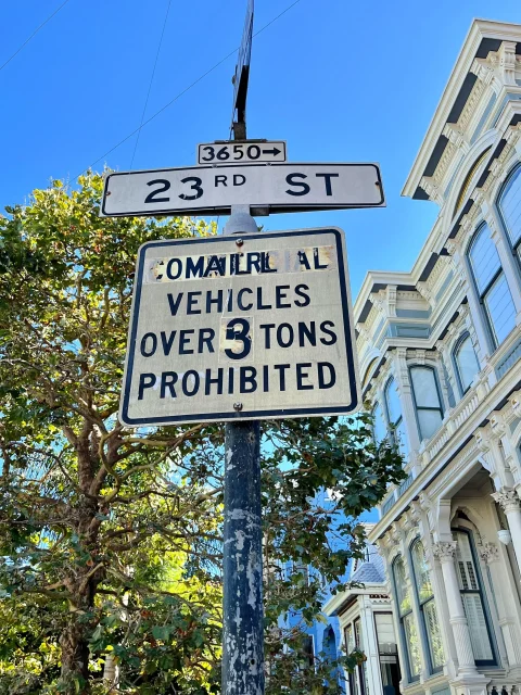 Street sign at the corner of 23rd Street and 3650 N; below it, a warning sign states "Commercial vehicles over 3 tons prohibited" in front of a historic building and trees.