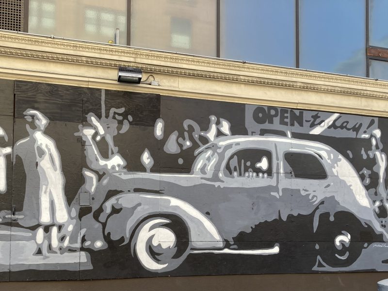 A grayscale mural of a vintage car and a person in a coat and hat, with the words "Open today" above them.