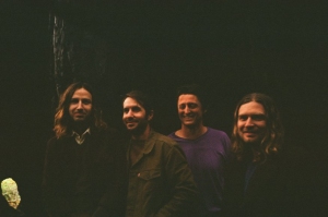 Four people stand together against a dark background, smiling.