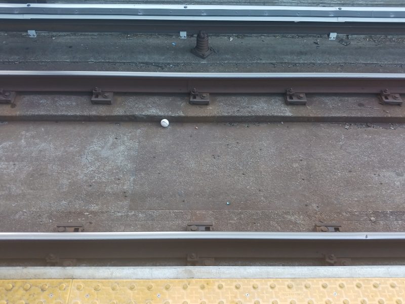 A railway track with a small white object in the center. Yellow tactile paving is at the edge of the platform.