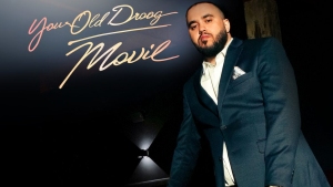 A person in a suit stands in front of a background featuring the text "Your Old Droog - Movin.