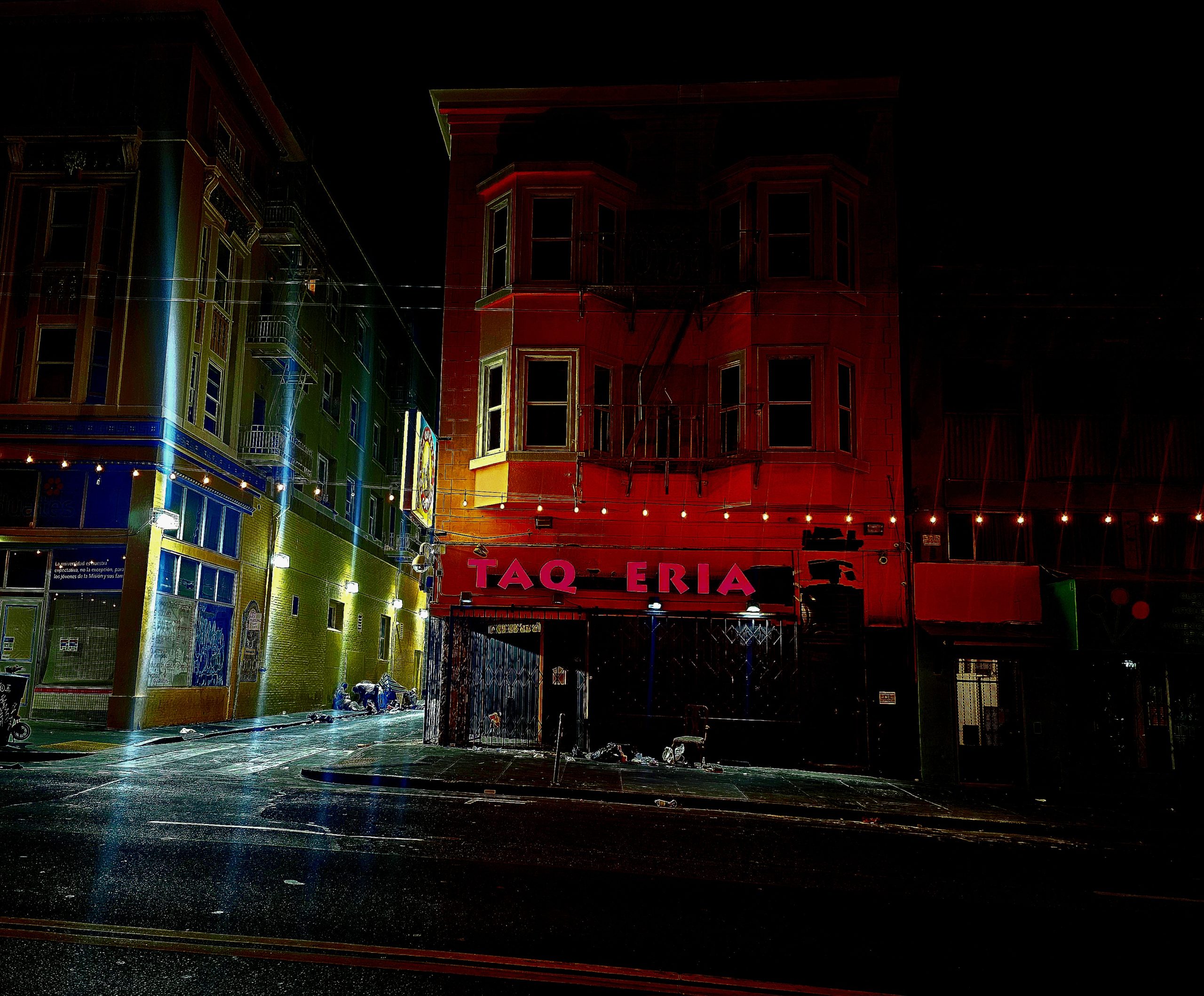 Street view of a taqueria at night, with dim lighting and colorful buildings on each side.