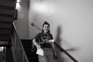 A person walking down stairs while holding a guitar and a piece of paper.