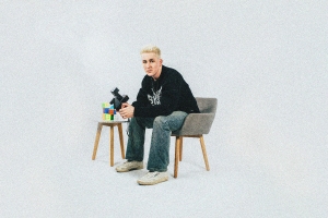 Person with light hair sitting in a gray chair, holding a camera, next to a small table with colorful stacked cubes.