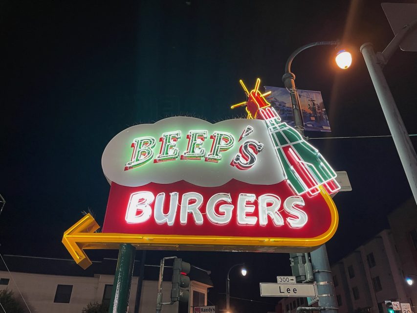 Neon sign for "Beep's Burgers," featuring a stylized rocket, illuminated at night.