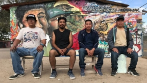 Four men are sitting on chairs in front of a colorful mural painted on a wall.
