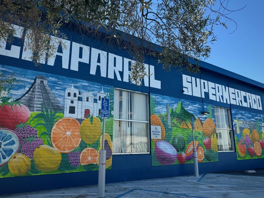 Colorful fruit mural on the exterior wall of Chaparral Supermercado, with blue sky above.