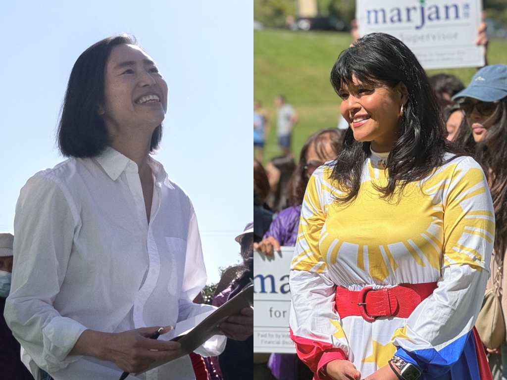 Two women standing outdoors, both smiling. The woman on the left holds a clipboard and wears a white blouse. The woman on the right wears a colorful dress with a sunburst design.