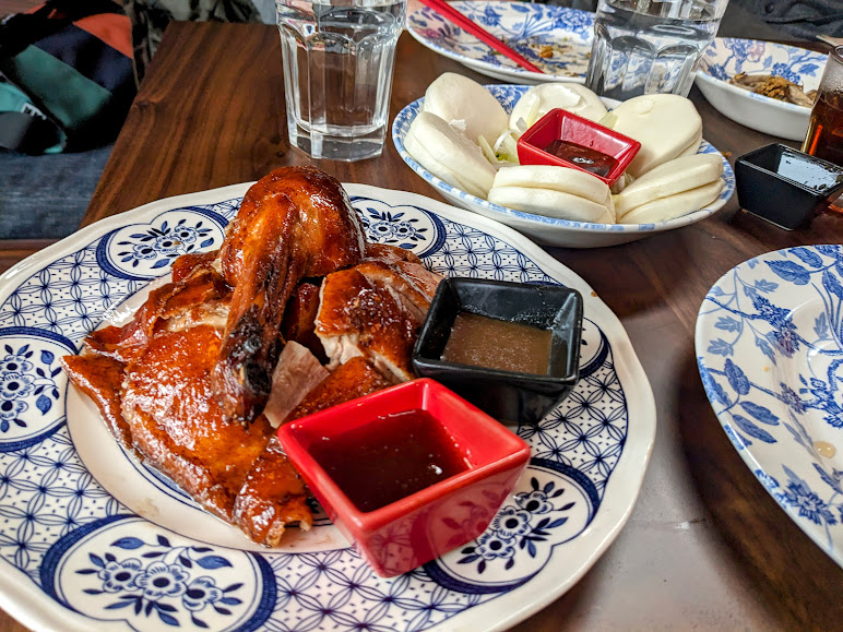 Roast duck with two dipping sauces on a plate, served with buns on the side. Glasses of water in the background.