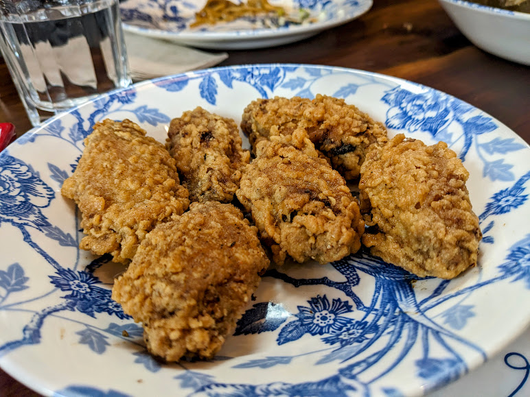 A plate of six crispy fried chicken wings on a blue and white floral-patterned dish, with a glass of water in the background.