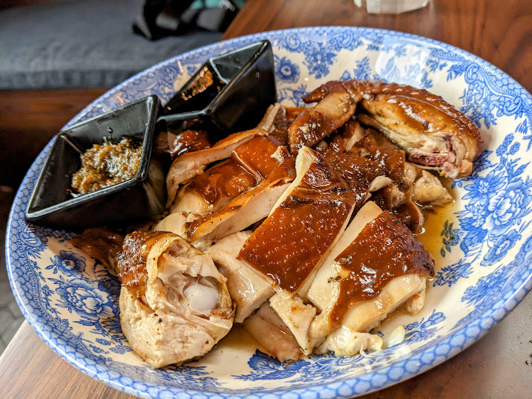 Roast chicken pieces served on a blue floral plate with two square containers of sauce.