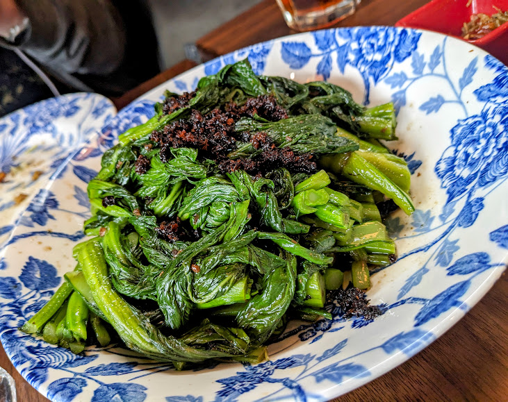 A plate of cooked greens topped with crispy bits, served on a blue and white patterned dish.