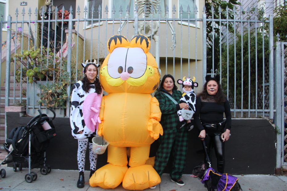 People in costumes, including a large Garfield inflatable, stand in front of a house with Halloween decorations.