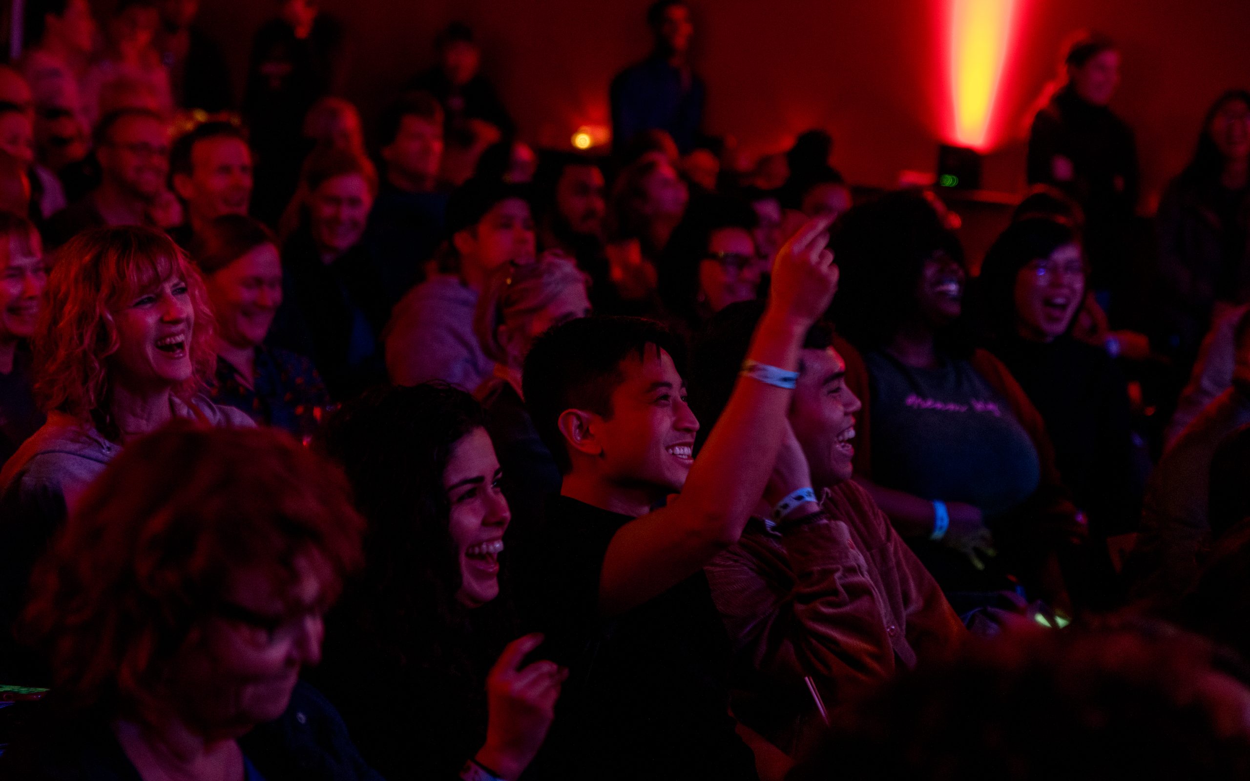 a darkened room full of people cheer and smile watching a reading