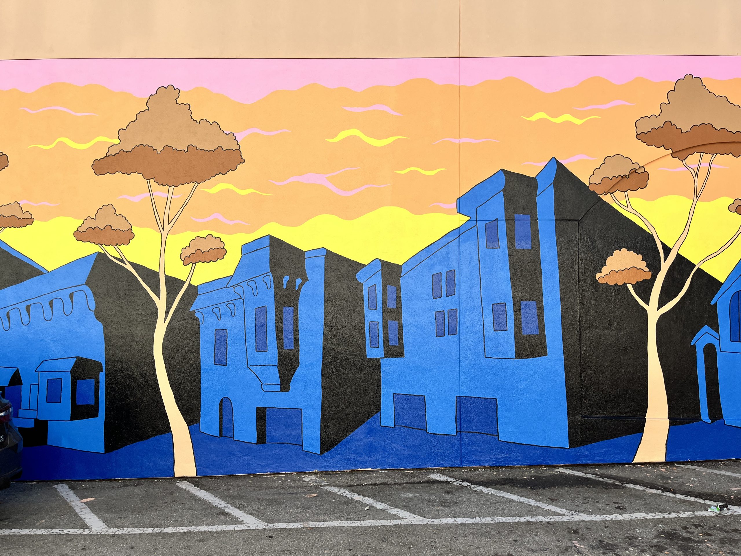 Colorful mural depicting stylized blue buildings with tall trees against a vibrant orange and pink sky.