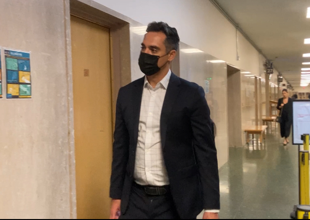 A person in a suit and mask walks down a hallway.