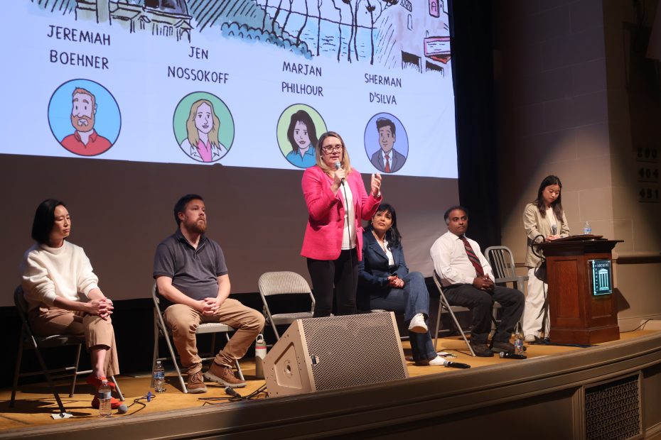 A panel discussion with five seated individuals and one standing speaker in a pink blazer. A person stands at a podium. Illustrated names are projected on a screen behind them.