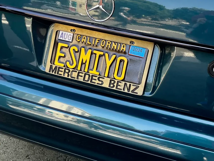 Close-up of a California license plate on a Mercedes Benz car, displaying the personalized text "ESMIYO.