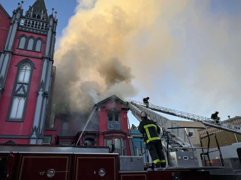 Firefighters embark on their fire mission to extinguish a blaze in a red building, skillfully using hoses and ladders. Smoke billows into the sky as a fire truck stands ready at the scene.