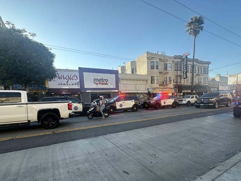 Several police vehicles with flashing lights are parked along a street near a jewelry store on Mission Street.