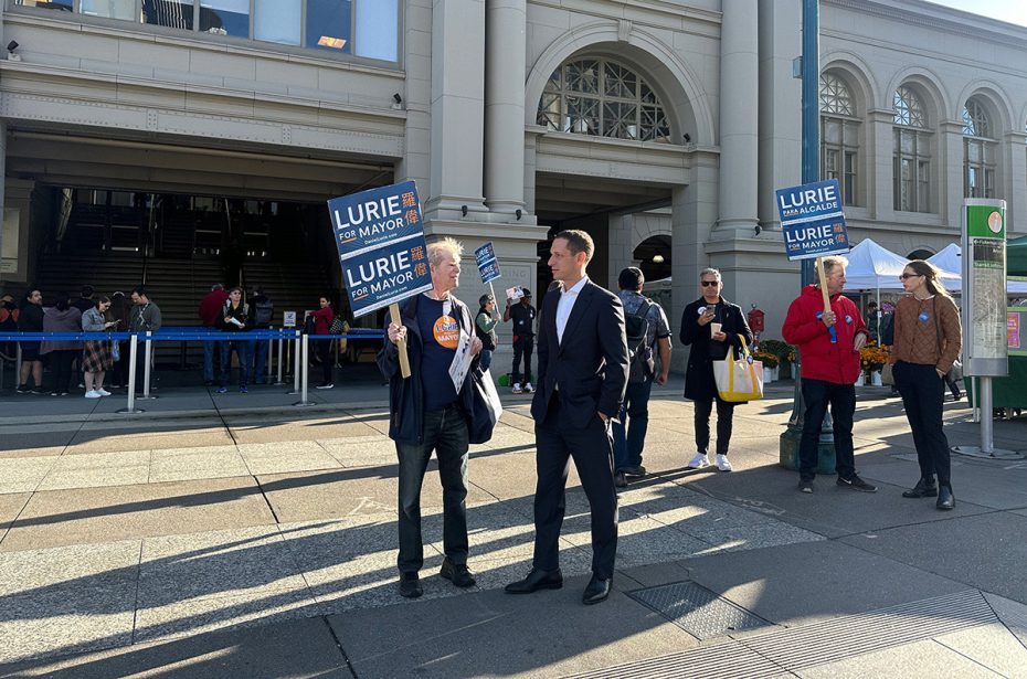People holding "Lurie for Mayor" signs stand outside a building amid a bustling crowd, signaling the energy of the SF election.