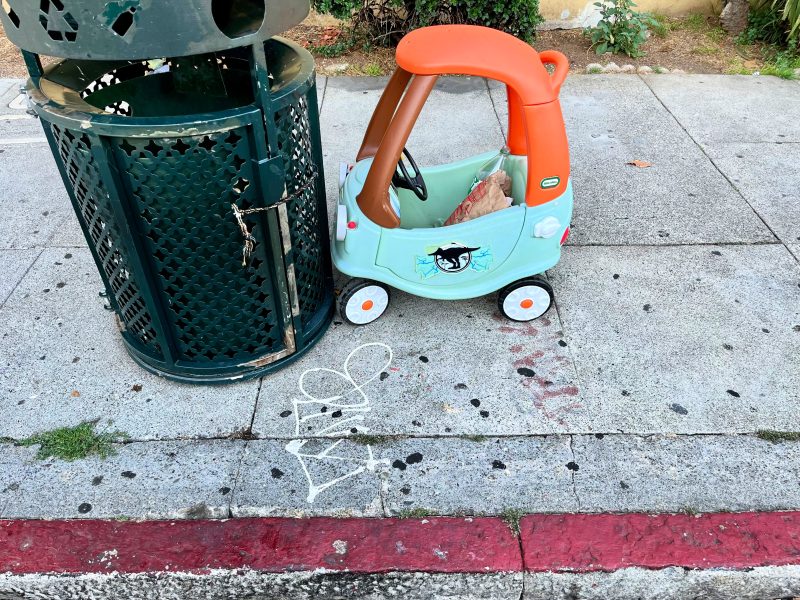A toy car is parked on a sidewalk next to a trash can. There is a hopscotch drawing on the concrete.