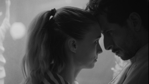 A black and white image of a woman and man facing each other closely, appearing to share an intense moment.