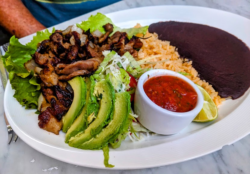 A plate of grilled meat, avocado slices, lettuce, sour cream, rice, beans, and a small bowl of salsa.