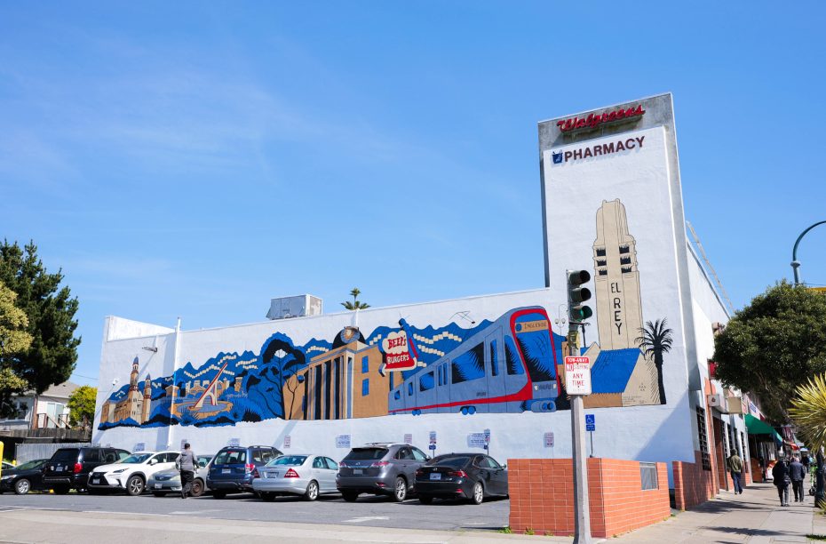 Wall mural depicting a train and cityscape on a Walgreens building, with a street scene and parked cars in the foreground.