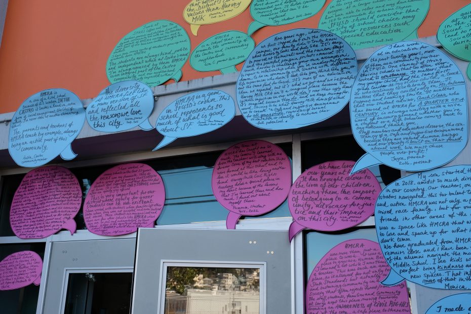 Colorful speech bubbles with handwritten messages are displayed on a building exterior around a door and windows.