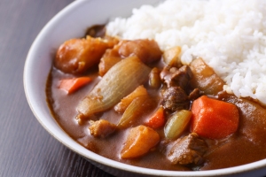 A plate with Japanese curry containing chunks of meat, carrots, potatoes, and onions served alongside white rice.
