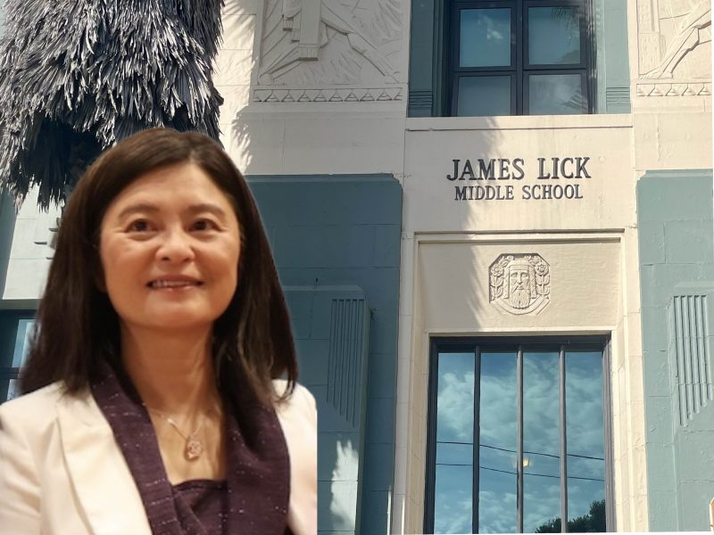 A woman in a white jacket stands in front of the entrance to James Lick Middle School.