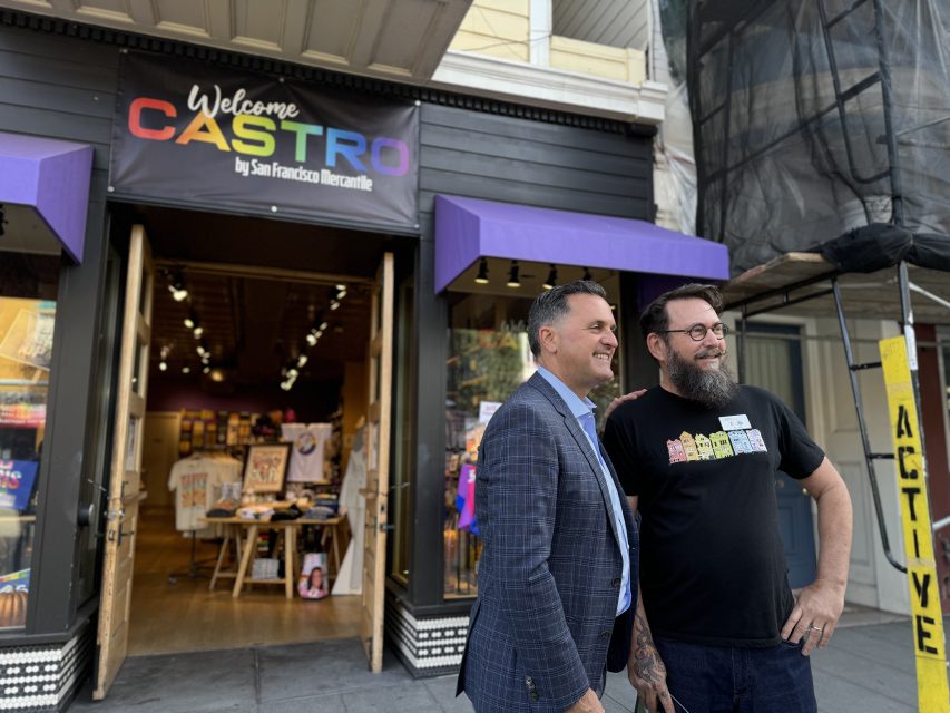 兩人站在三藩市商品店（San Francisco Mercantile）前，店鋪入口上方有一個「歡迎來到Castro」的招牌。