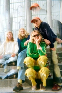 Four people with casual attire and varied hairstyles pose on stairs in front of a building.