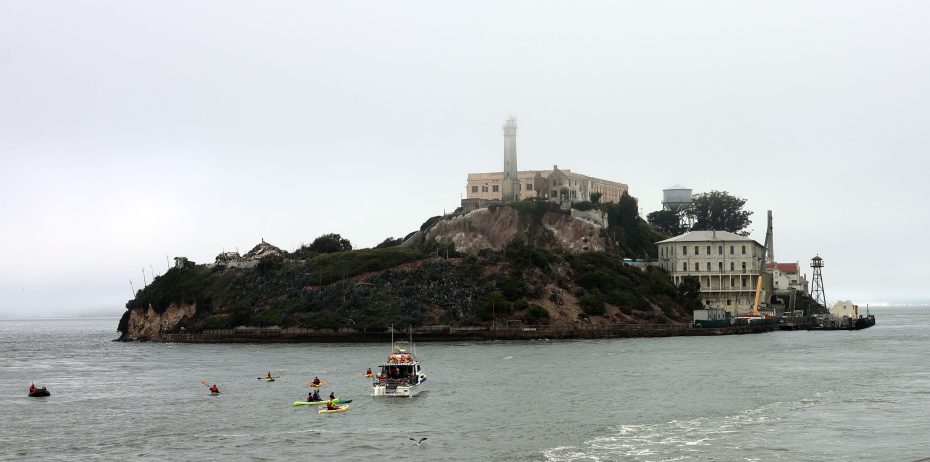 View of Alcatraz Island with several small boats and a larger boat in the surrounding waters on an overcast day.
