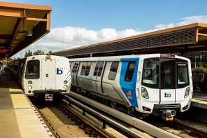 Two BART trains at a station platform under a partly cloudy sky.