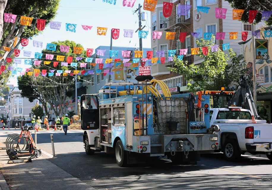 Utility trucks parked on a street under bright, colorful banners indicate an ongoing operation. Workers in the background assess the situation, diligently addressing a potential gas leak to ensure safety for all.