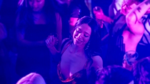 A woman dances in a dimly lit club, surrounded by people and colorful lighting.