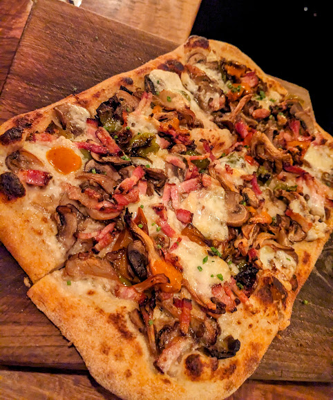 Close-up of a rectangular pizza topped with mushrooms, cheese, and bacon on a wooden board.