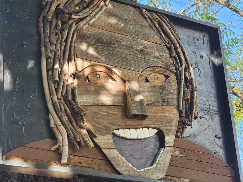 A wall art piece made from wood and branches depicts a smiling face with leaves in the background.