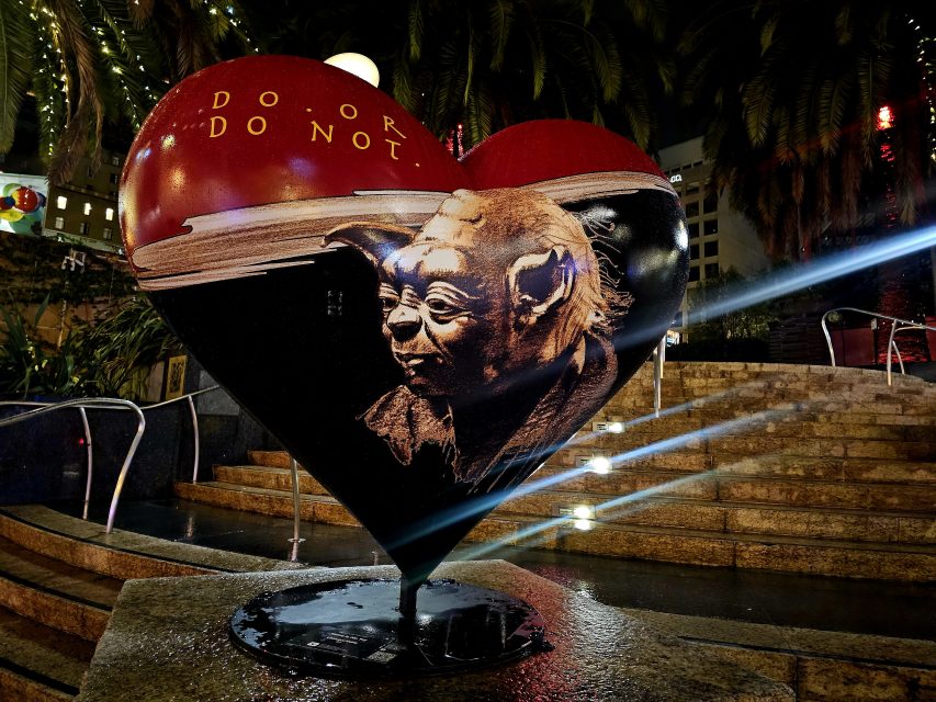 Heart sculpture in a city square, featuring Yoda from Star Wars with the phrase "Do or do not." Surrounded by steps and palm trees, illuminated at night.