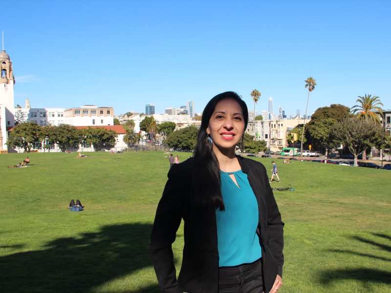Born in Nicaragua, Alice Ruiz poses in a black blazer with a cityscape in the background at Dolores Park.