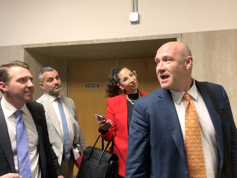 Four people in business attire stand talking in a hallway near a door.